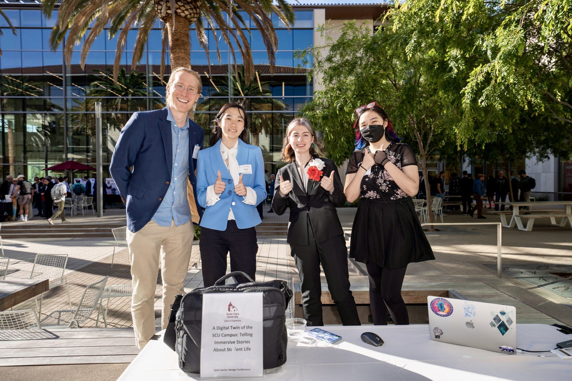 Four people at an outdoor project display with a laptop.
